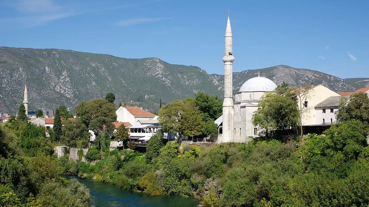 The rebuilt Old Bridge of Mostar arching over the green Neretva, stone houses and a minaret rising behind