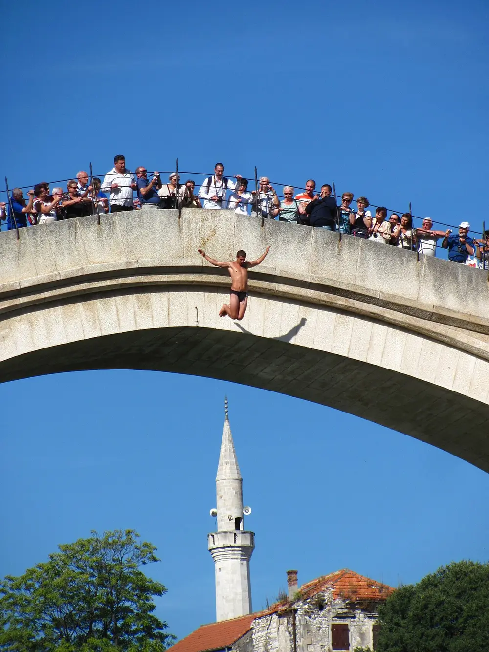 A diver poised on the parapet of the Old Bridge in Mostar above the Neretva, watched by a crowd
