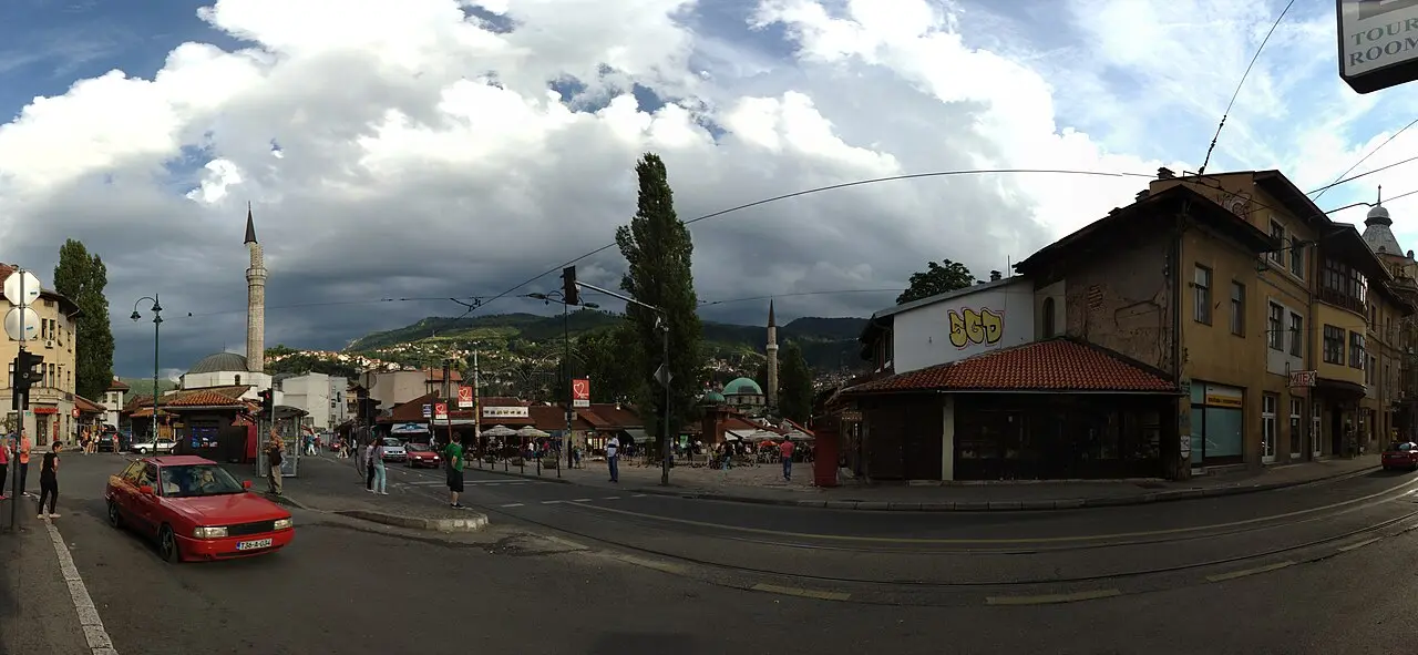 The Ottoman bazaar of Baščaršija in Sarajevo seen from above, low tiled roofs, minarets and green hills behind