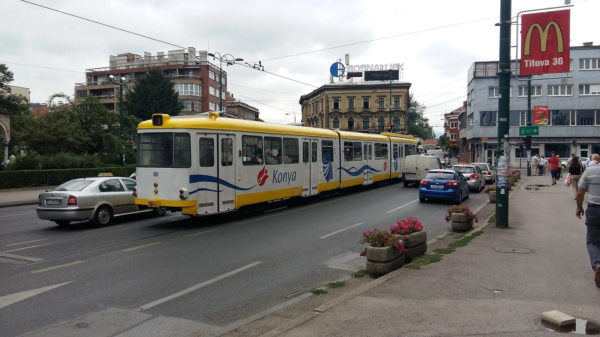 A Sarajevo tram running along the valley corridor with apartment blocks and hills behind