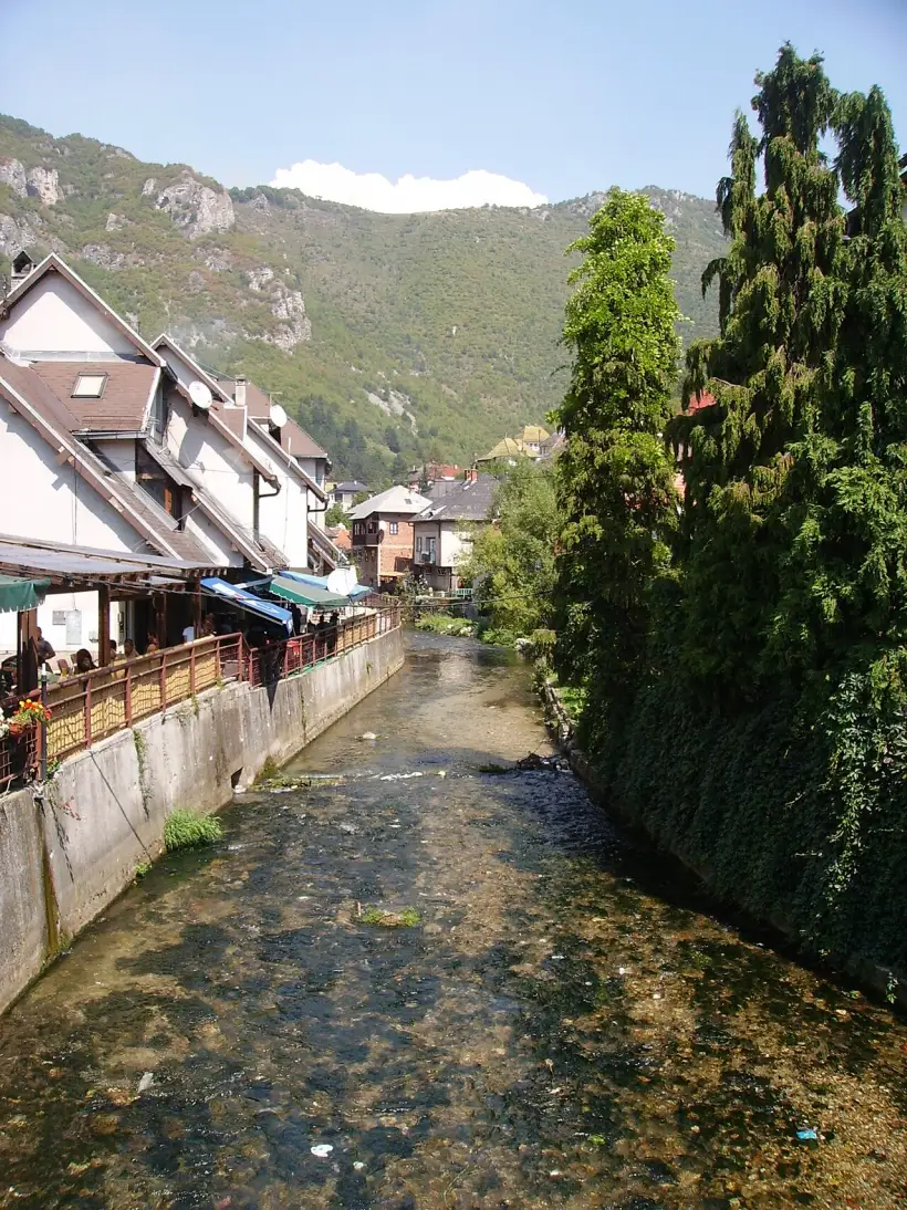 The Lašva river running below cafe terraces in the old town of Travnik, wooded hills behind