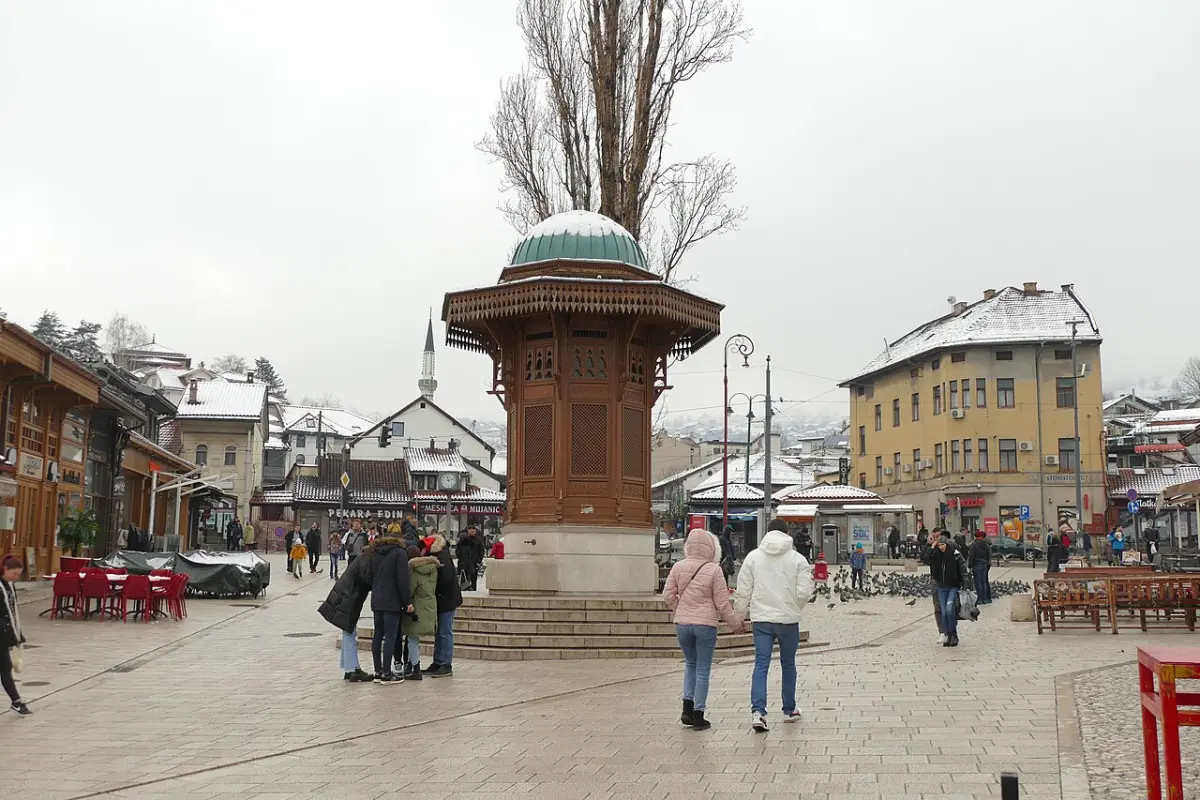 The octagonal wooden Sebilj fountain on Baščaršija square with pigeons on the cobbles and bazaar rooftops behind