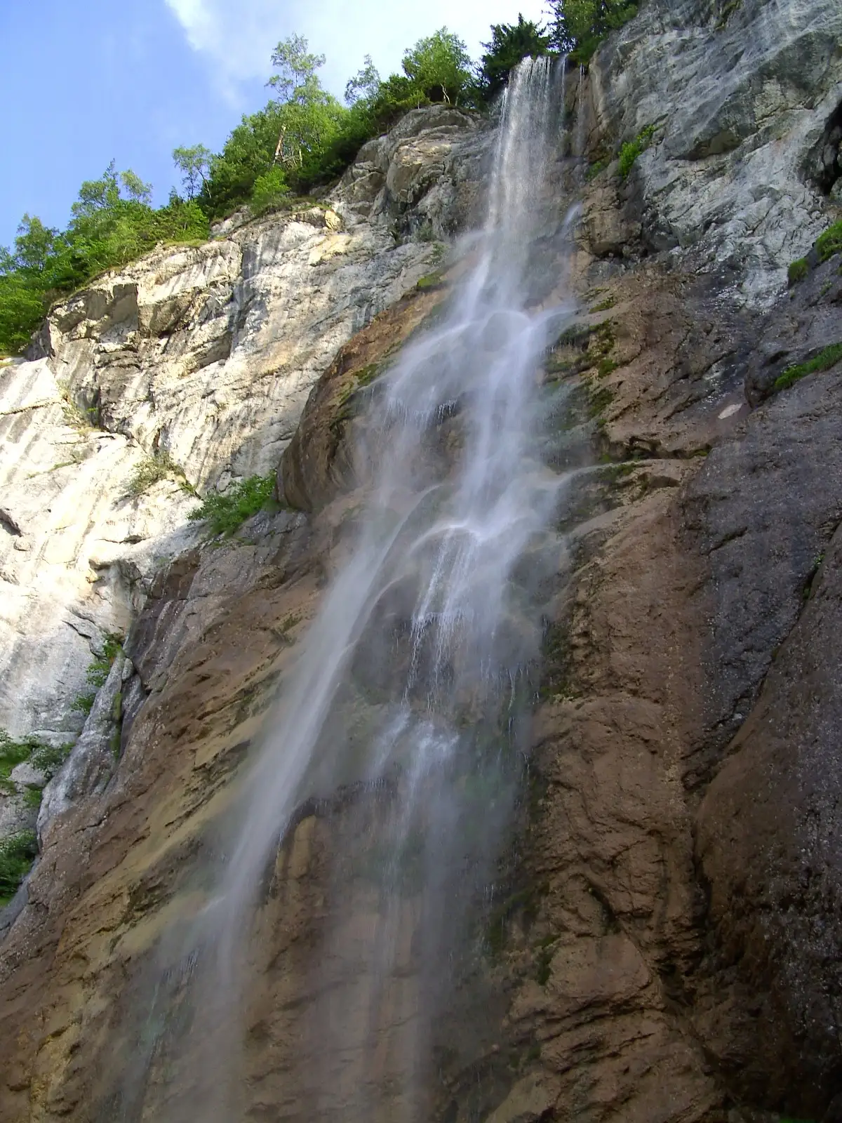 Skakavac waterfall seen from the base, the full height of the limestone cliff visible through wet forest