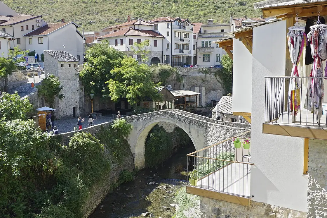 The small Ottoman Crooked Bridge over the Radobolja stream in Mostar old town, stone houses and a souvenir stall around it, where the route ends