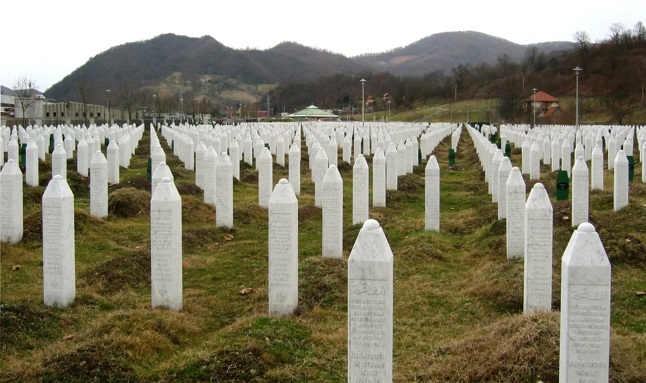 Rows of tall white marble grave markers at the Srebrenica-Potočari cemetery beneath bare winter hills