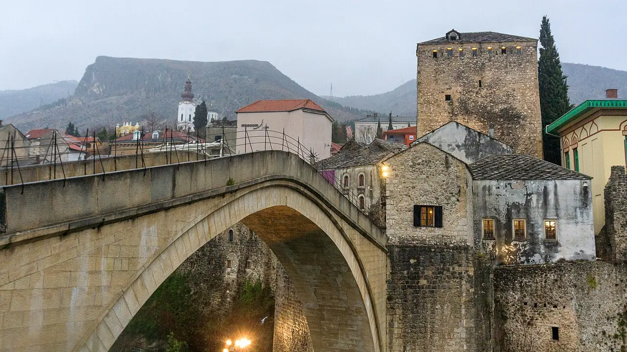The Ottoman Old Bridge of Mostar arching between the old town houses and the stone diving tower under soft light