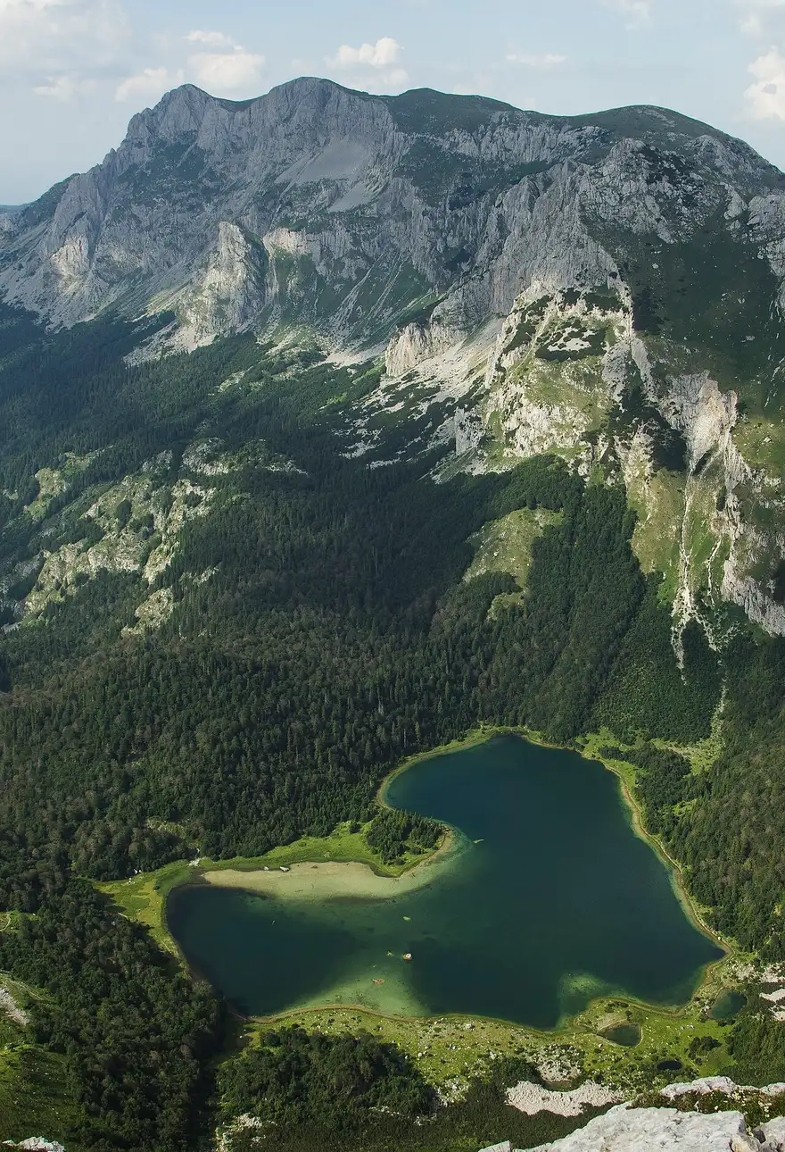 The grey massif of Maglić towering over the deep green Trnovačko lake in its forested basin, seen from above