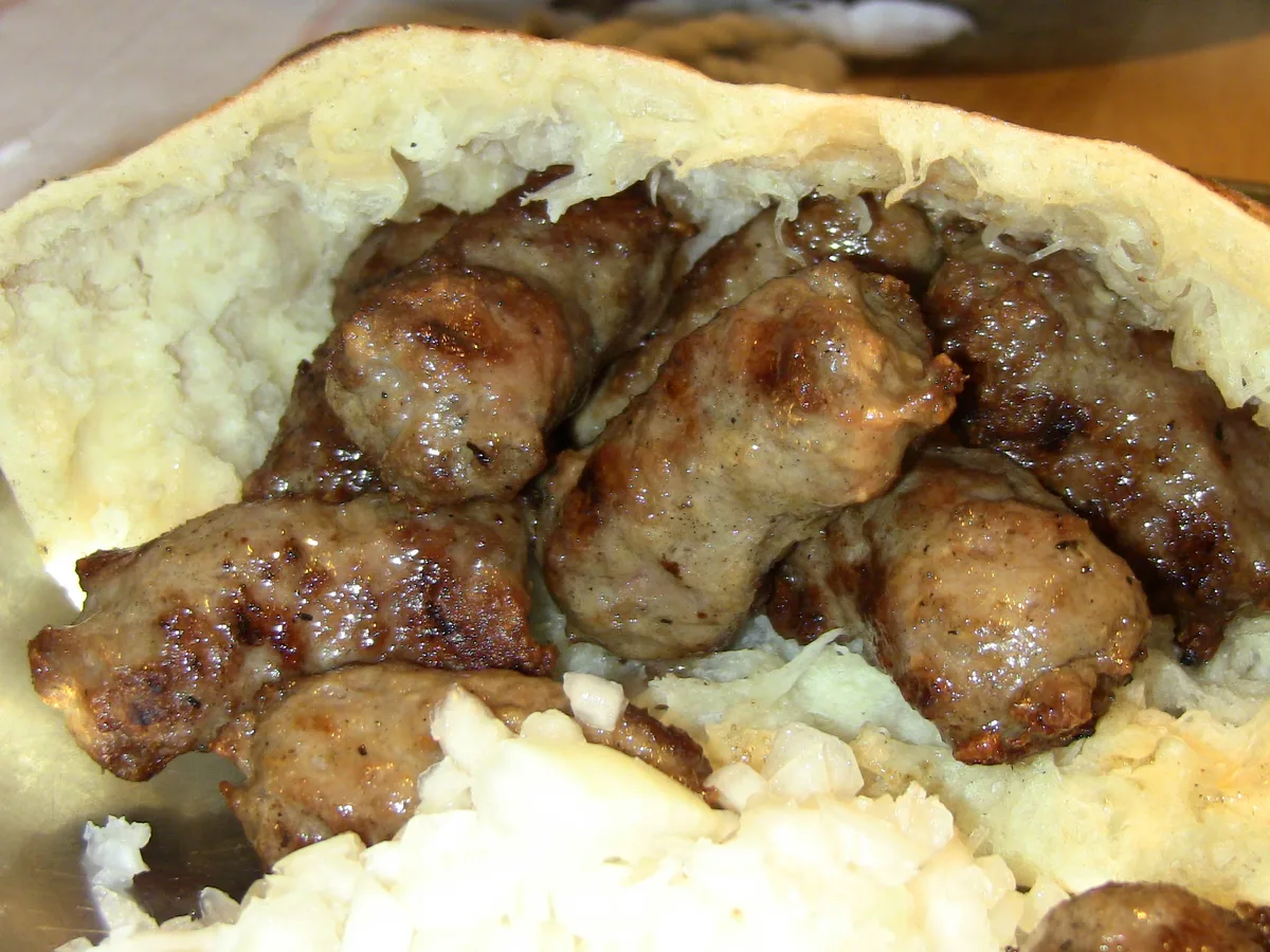 A portion of Sarajevo ćevapi: grilled beef sausages in somun flatbread with chopped raw onion