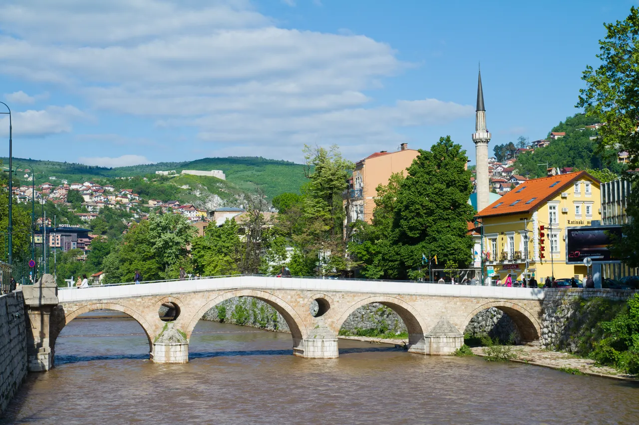 The Ottoman stone Latin Bridge over the Miljacka in Sarajevo, with the assassination-corner building and a minaret behind