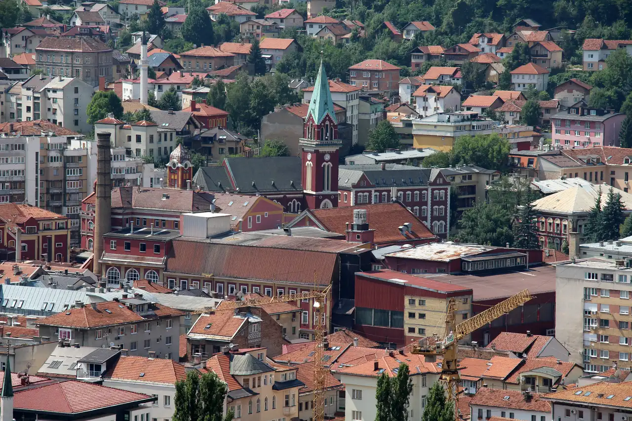 Elevated view over Sarajevo's terracotta roofs from the fortress, with the cathedral spire and a minaret rising among the buildings