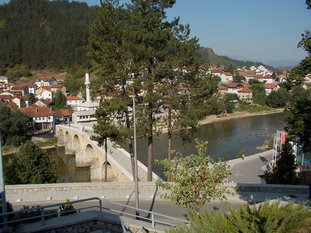 The Ottoman stone bridge over the green Neretva river in the town of Konjic, with a minaret and wooded hills behind