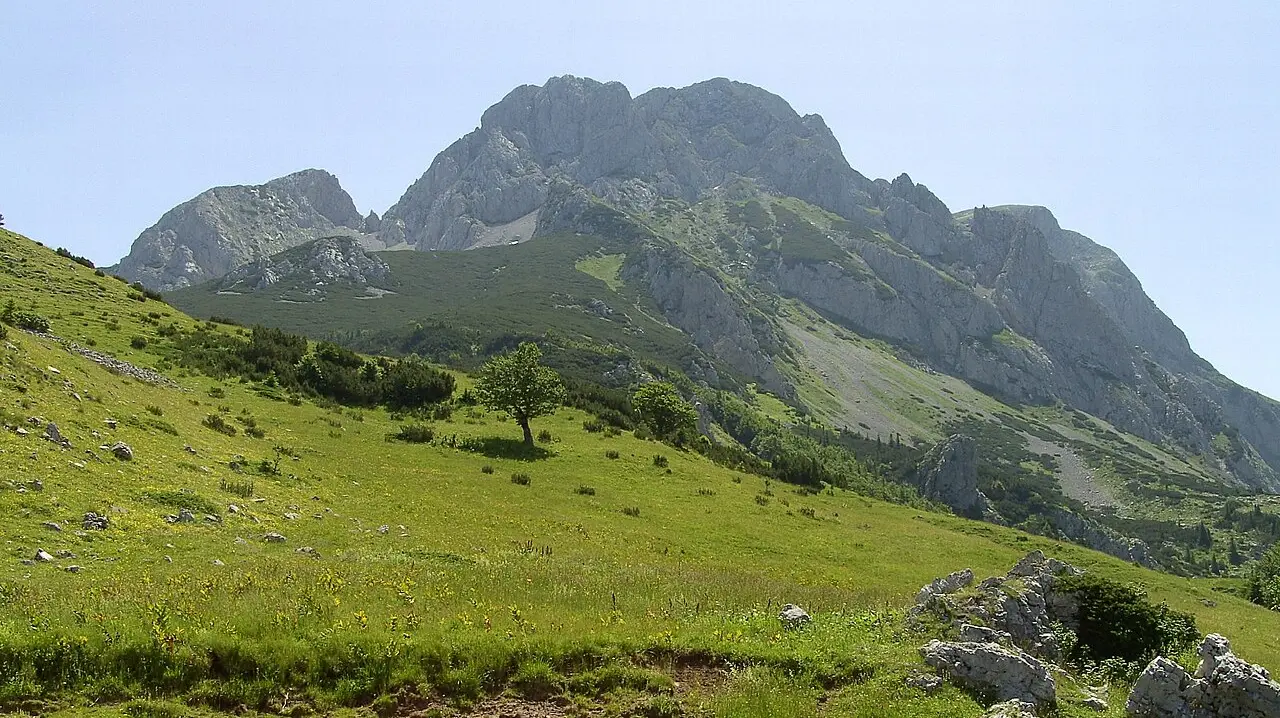 The rocky pyramid summit of Maglić, Bosnia's highest peak, rising above green alpine slopes under a clear sky