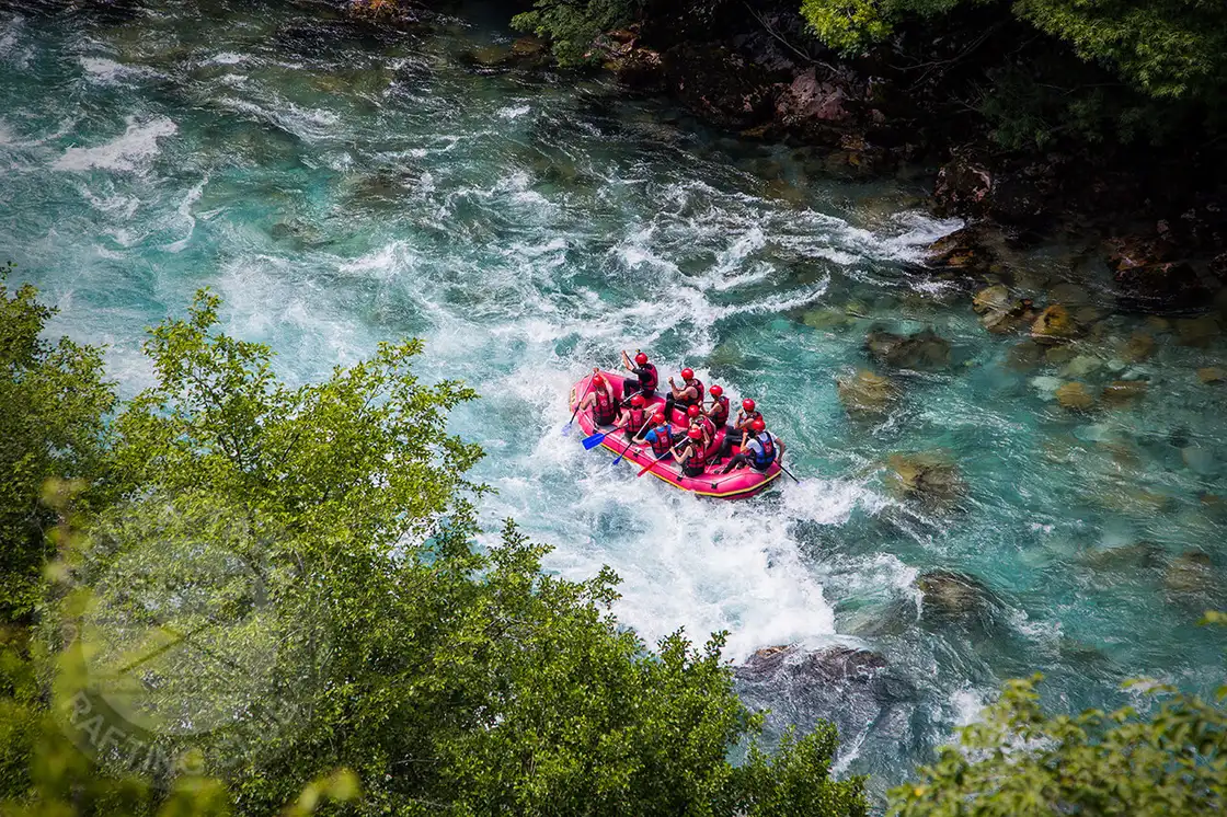 A raft of paddlers in helmets and life jackets working through white water on the Tara river between forested banks