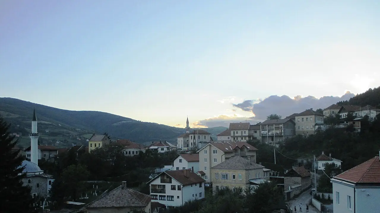 The red roofs and minarets of Travnik old town at dusk, wooded hills rising behind