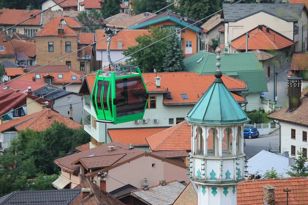 A cable car cabin climbing above the old town of Sarajevo with a minaret in the foreground