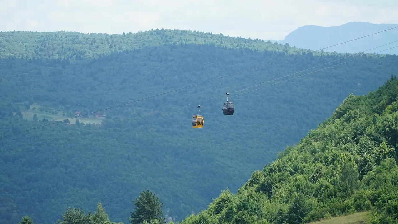 Two gondola cabins of the Trebević cable car, one yellow and one dark, crossing the forested valley above Sarajevo