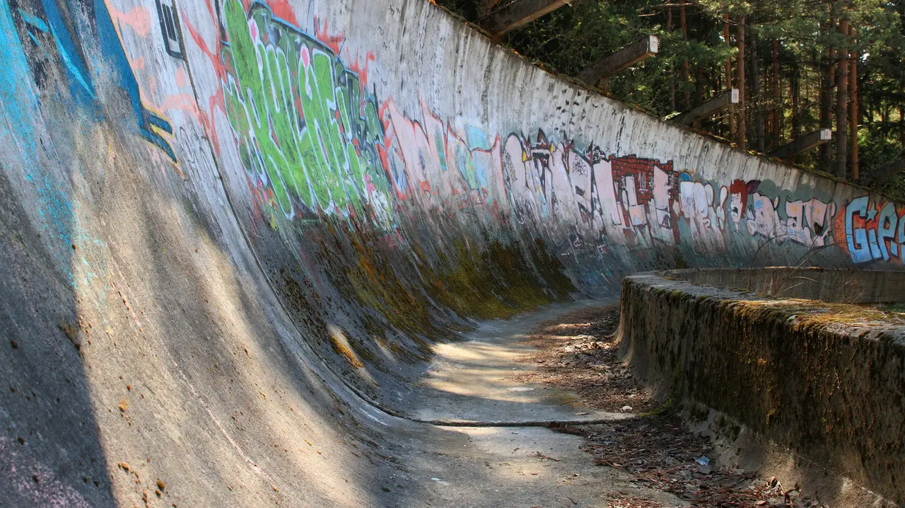 The banked concrete curve of the abandoned 1984 Olympic bobsled track on Trebević, covered in bright graffiti, forest behind