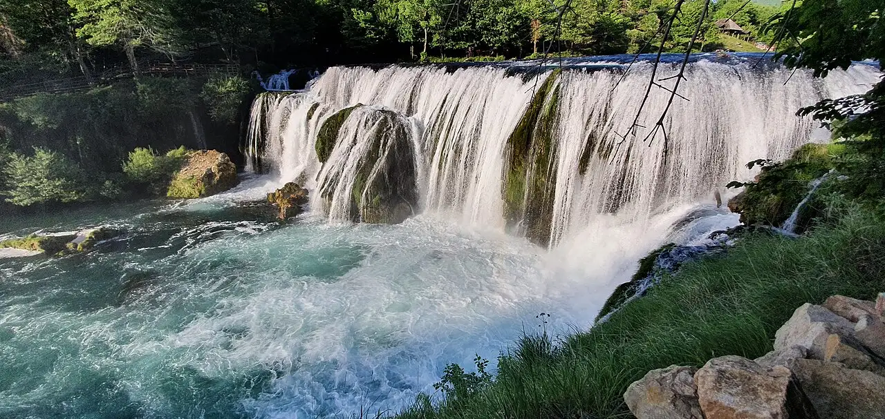 Wide view of Štrbački buk, the Una spilling over a broad terraced tufa ledge in several white curtains