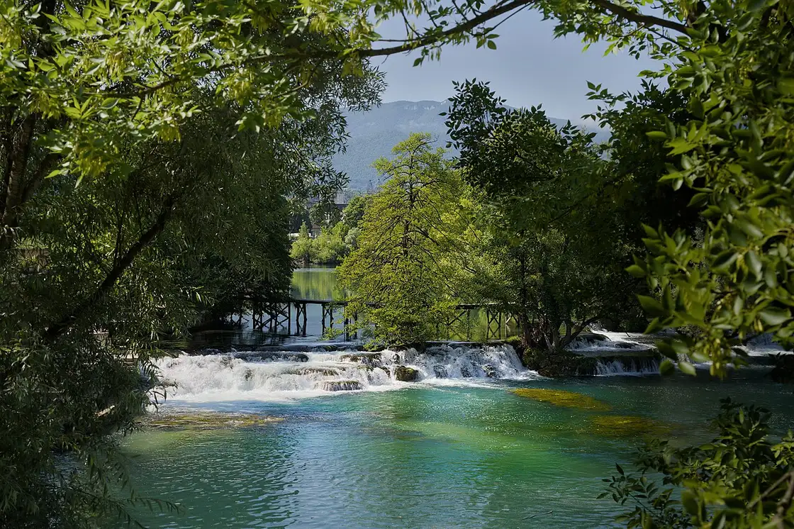 The emerald-green Una river running clear over a shallow bed near Bihać, wooded banks on either side