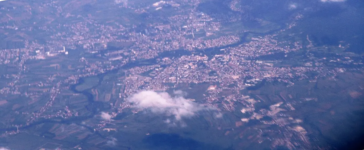 The town of Bihać seen from the west, low buildings along the green Una river with wooded hills behind