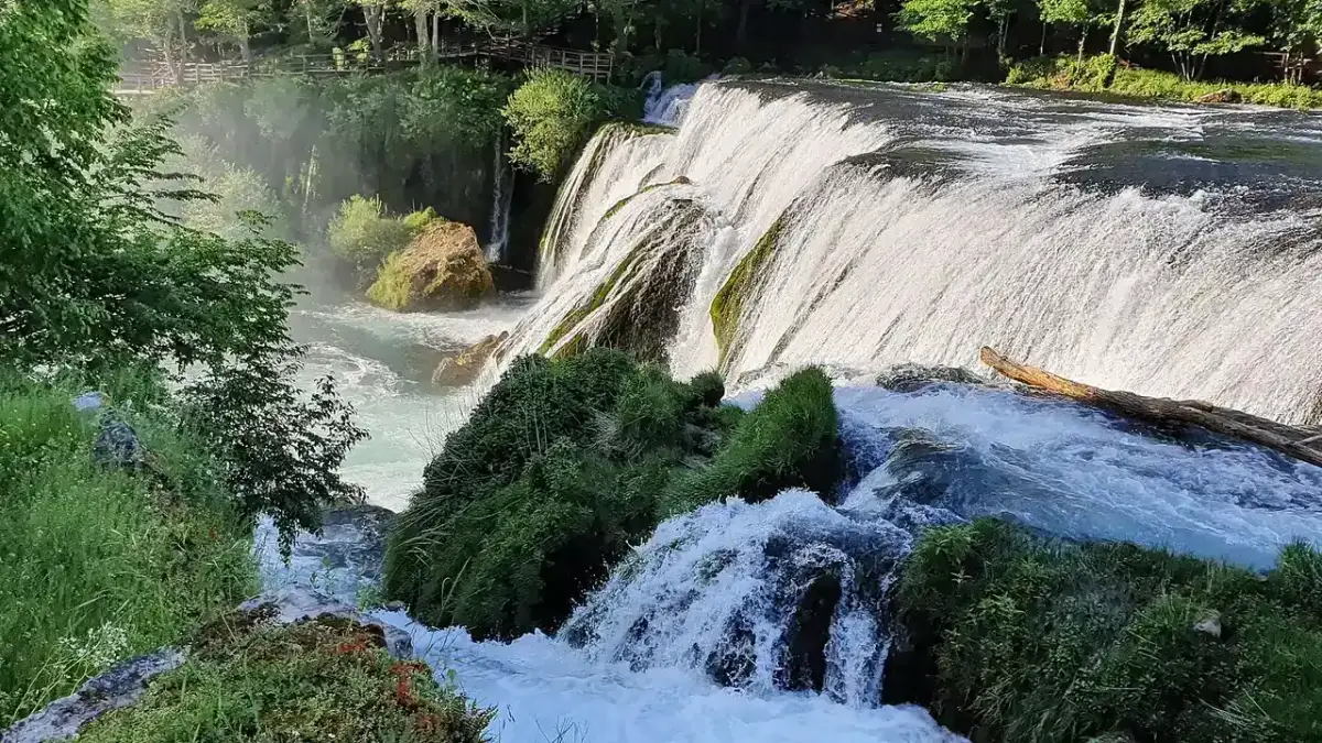 Štrbački buk, the Una spilling in wide white curtains over a broad staircase of tufa steps, green forest all around