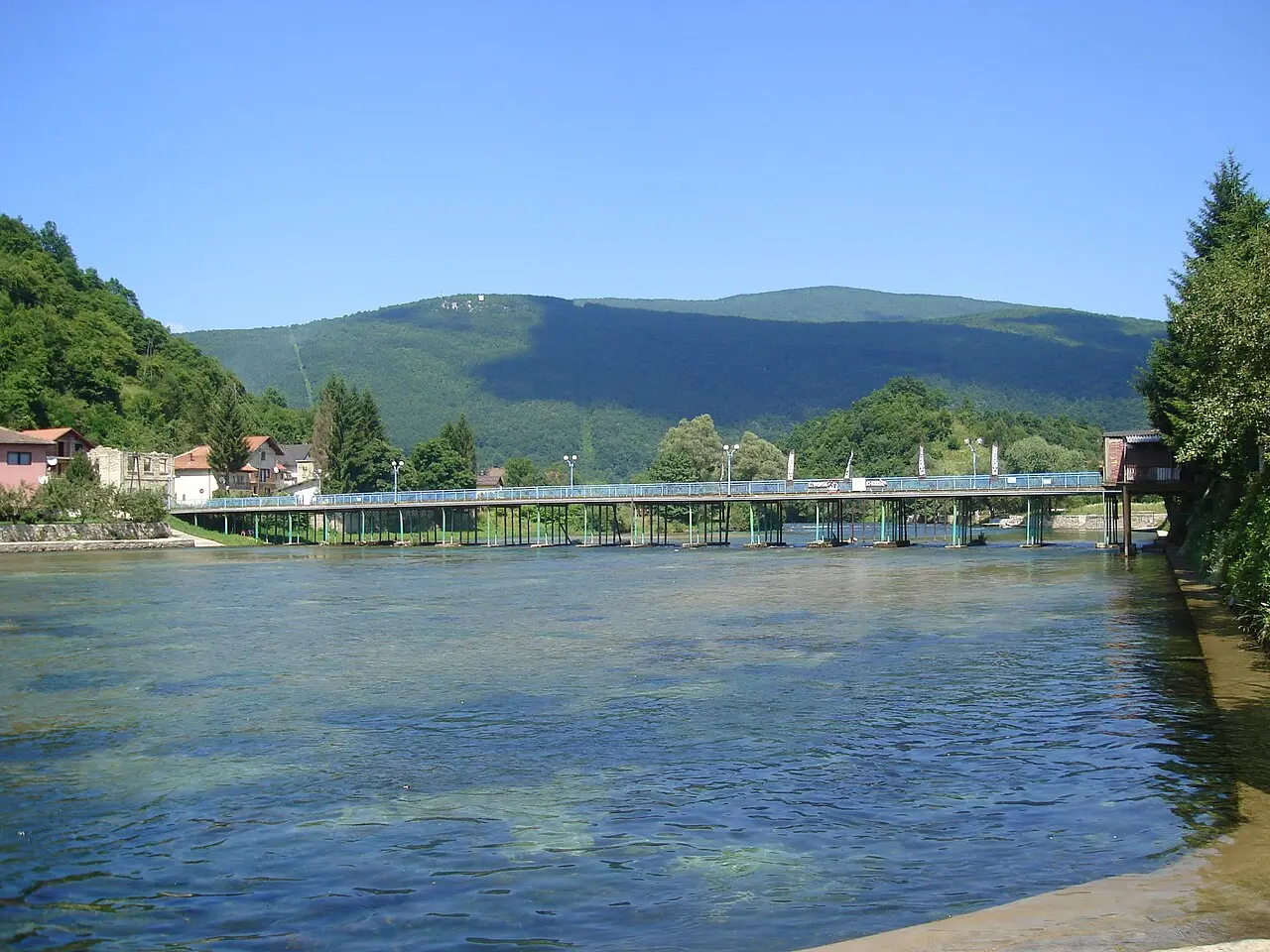An old bridge over the clear Una river at Kulen Vakuf, village houses and green hills beyond