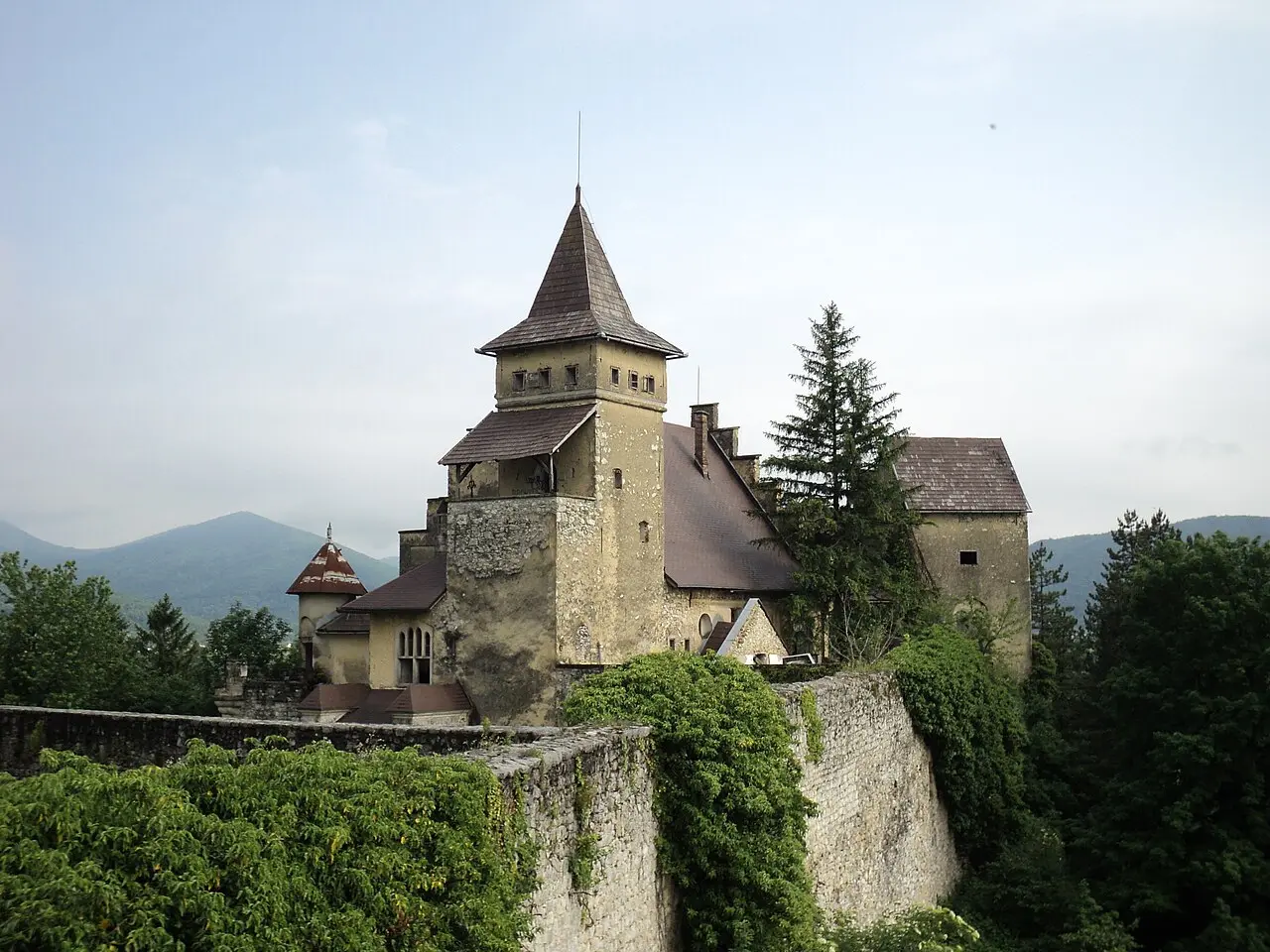 The tall stone walls and tower of Ostrožac castle rising from trees on a hillside above the Una valley