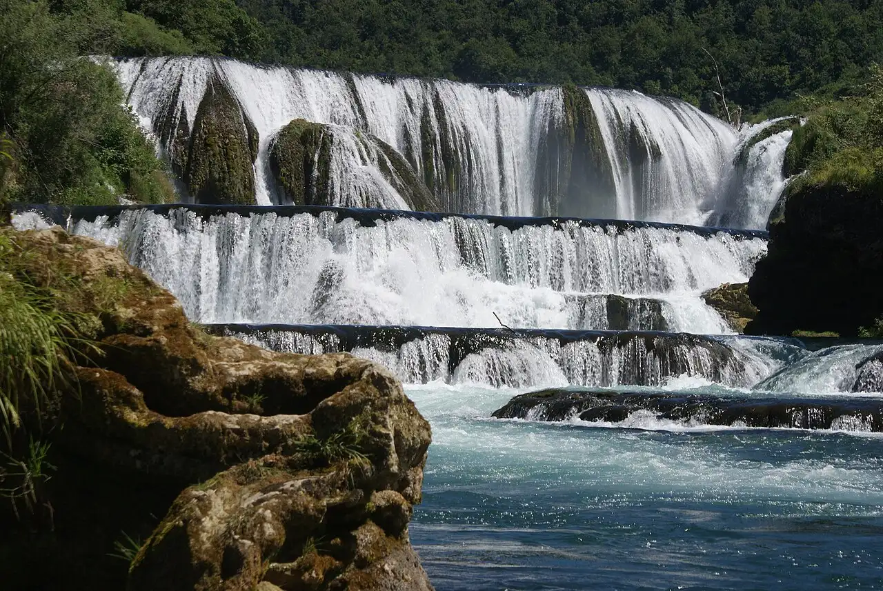 Štrbački buk seen from the side, the Una dropping in several white curtains over broad tufa ledges into a green pool