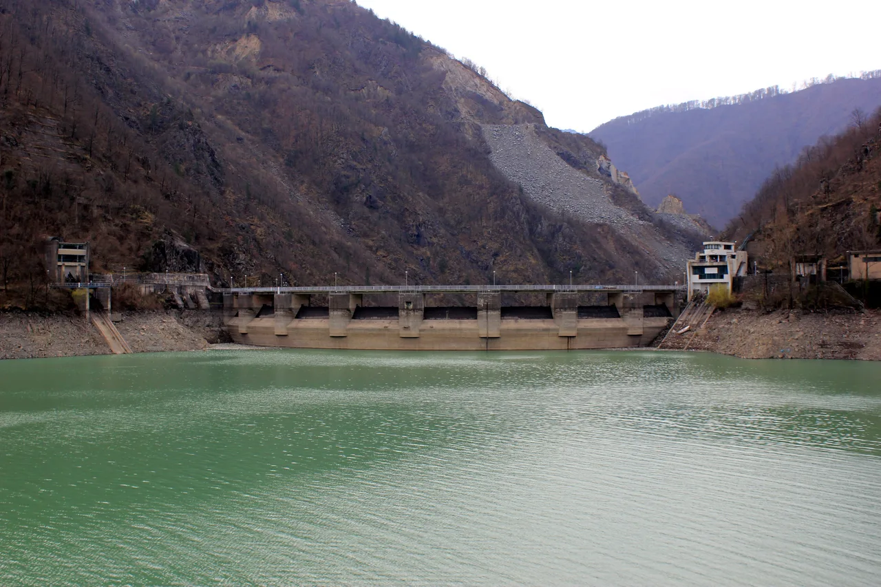 The concrete dam holding back the Neretva river to form Jablanica Lake, forested hillsides behind