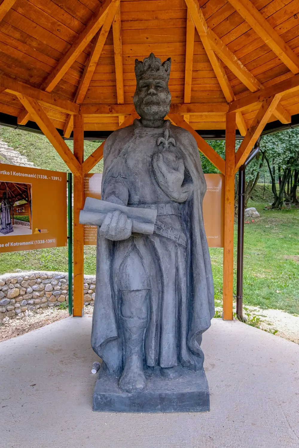 A grey statue of the medieval Bosnian king Tvrtko I Kotromanić under a wooden gazebo in the Ravne 2 park