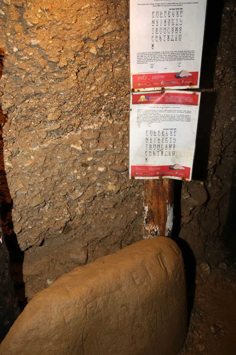 Information boards inside the Ravne tunnels showing runic symbols and pyramid diagrams beside a rough conglomerate wall