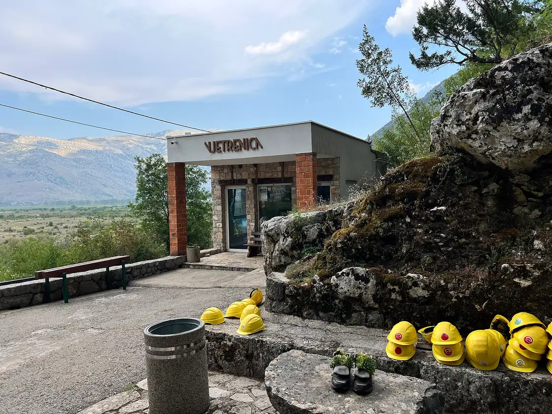 The Vjetrenica ticket office building above Popovo polje with rows of yellow safety helmets laid out on the stone wall outside