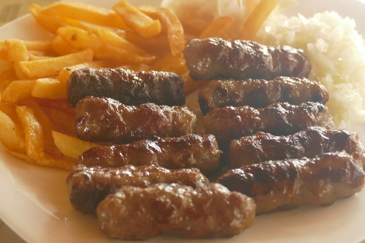 A plate of grilled Bosnian ćevapi minced-meat links with chips, rice and chopped raw onion