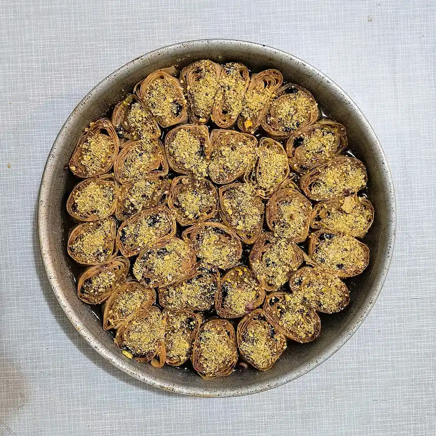 A round baking tin of djul pita, a Bosnian rolled pastry cut into pieces and topped with crushed nuts in syrup