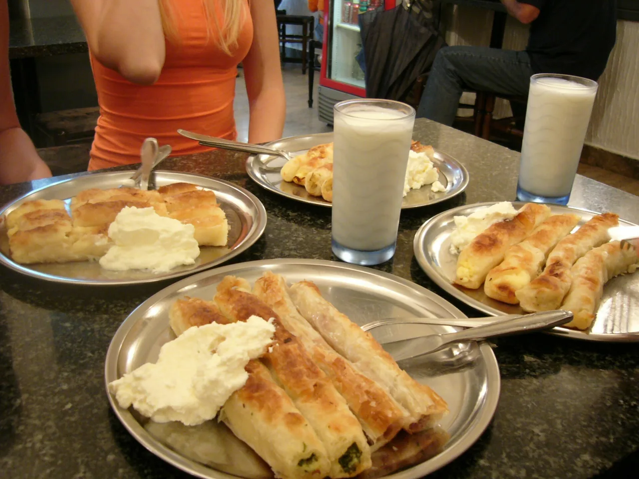Metal plates of Bosnian pita, coiled filo pastries filled with cheese and greens, served with dollops of kajmak and glasses of ayran