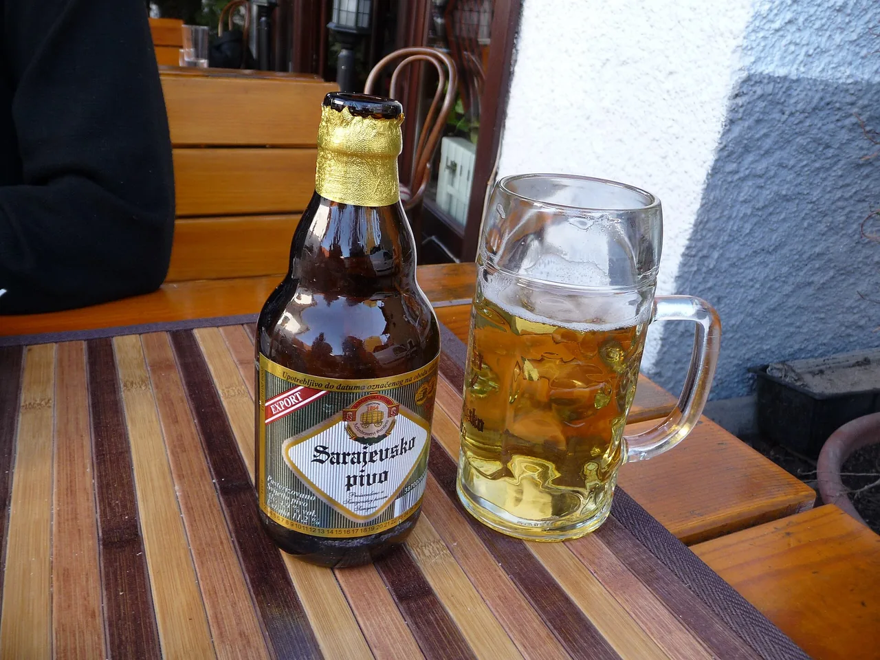 A bottle of Sarajevsko pivo beside a full glass mug of lager on a wooden table