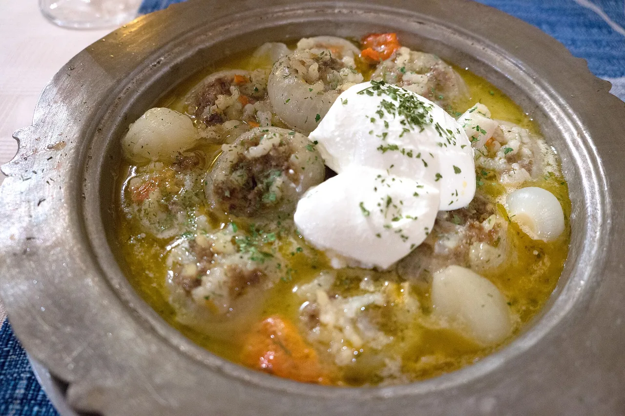 A pewter dish of sogan-dolma, whole onions stuffed with minced meat and rice in a golden broth, topped with a spoon of yoghurt