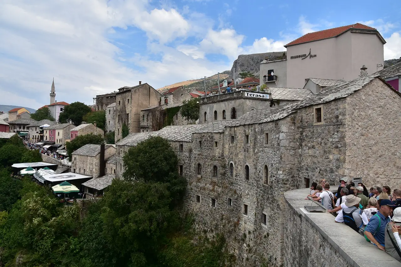 Stone-roofed Old Town houses in Mostar with packed restaurant terraces and a Terasa sign, seen from the bridge parapet