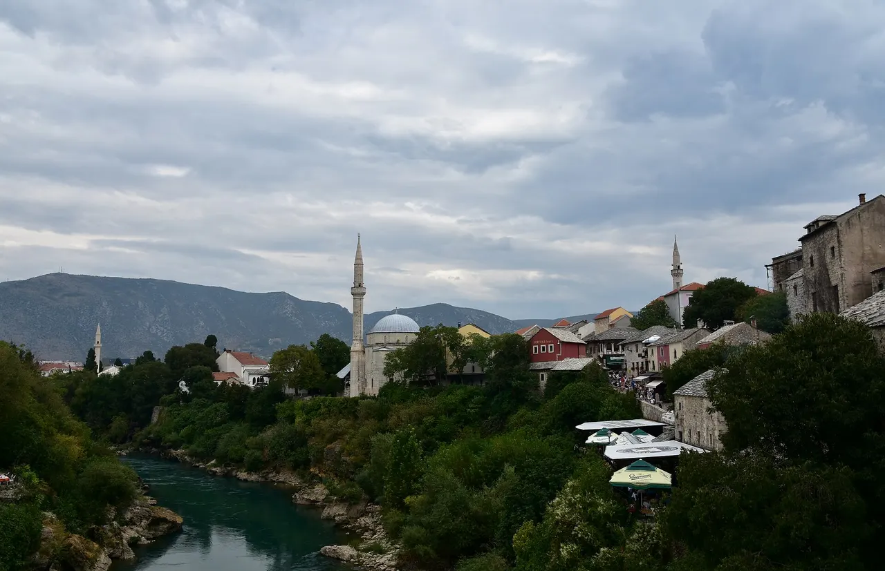 Riverside restaurant terraces under white umbrellas on the Neretva below the Koski Mehmed-Pasha mosque in Mostar