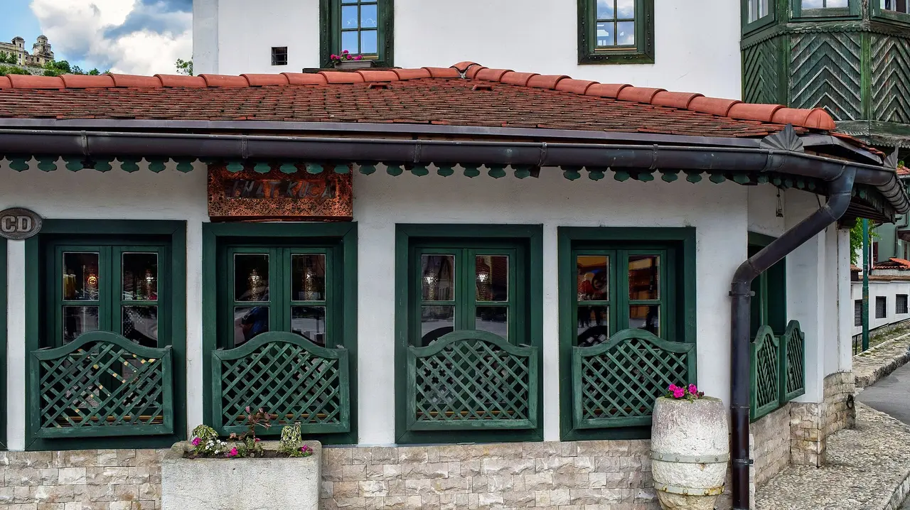 The white and green Ottoman-style facade of Inat kuca restaurant in Sarajevo with a copper sign above the shuttered windows