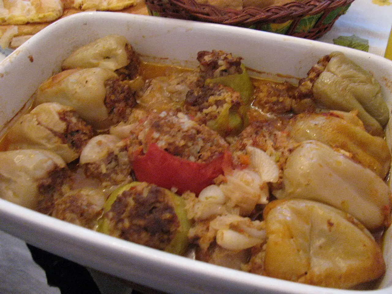 A white dish of stuffed peppers and stuffed onions baked in their own sauce, Bosnian style