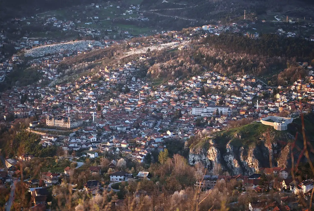 The Vratnik quarter of Sarajevo seen from above at dusk, red roofs climbing the hillside with the Yellow Bastion on the ridge