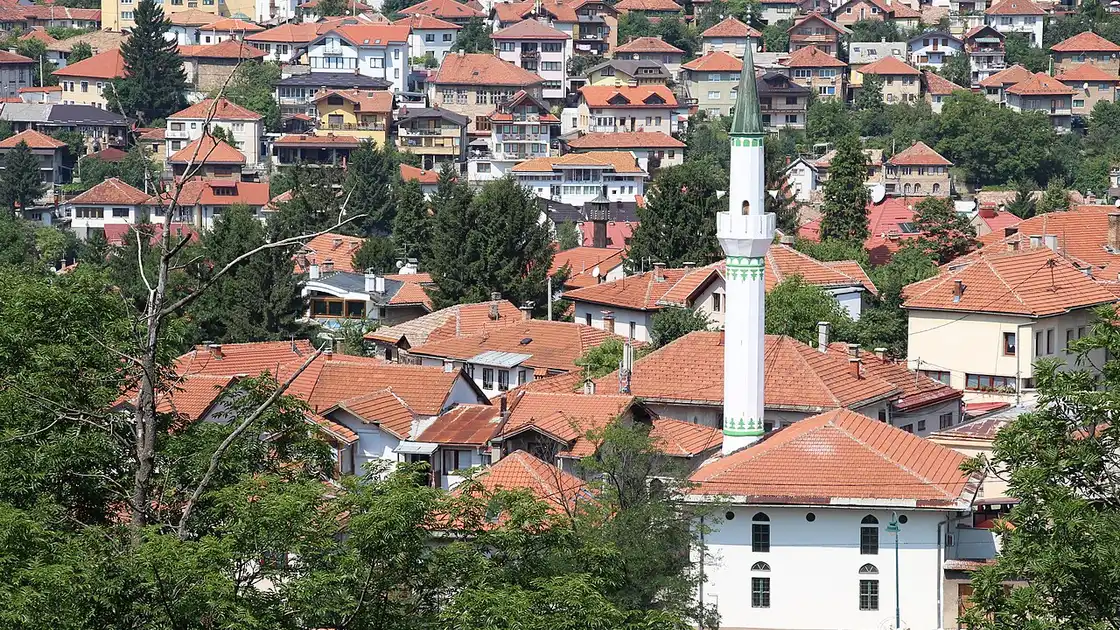 The red-tiled roofs and a slender minaret of old Sarajevo climbing the wooded hillside of its valley