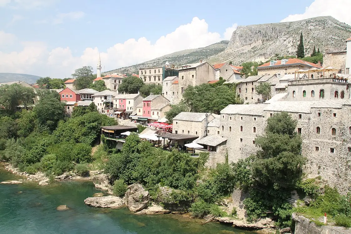 The old stone houses of Mostar along the turquoise Neretva with café terraces and a bare mountain behind