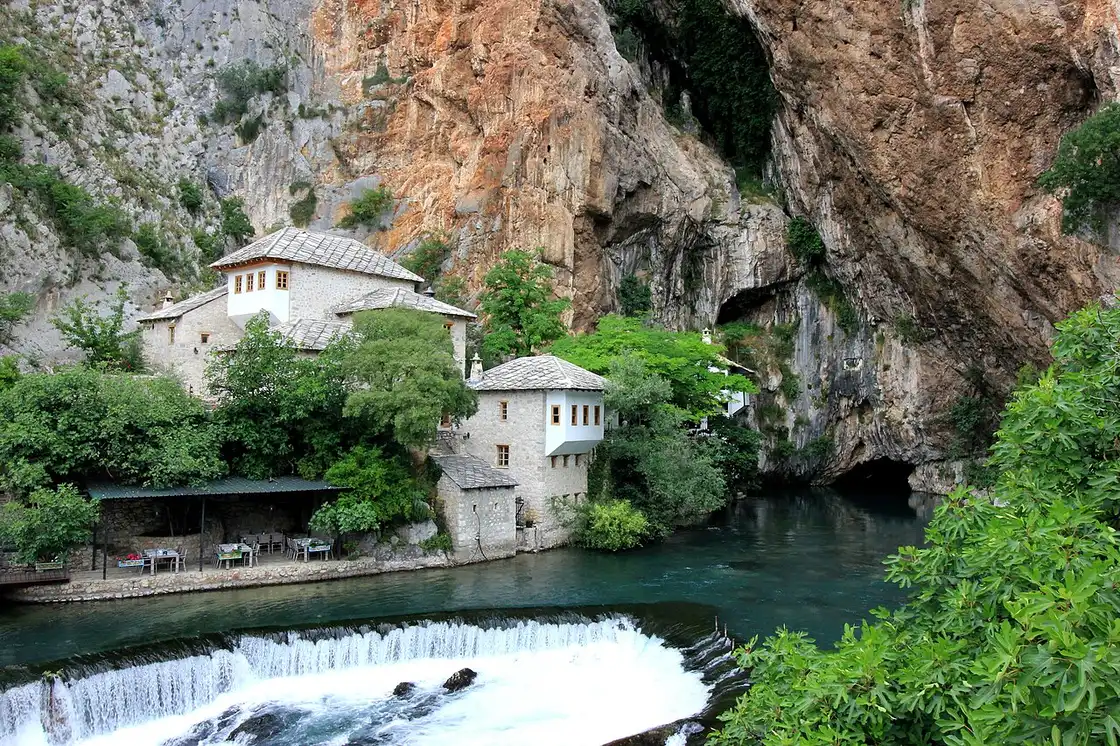 The white Blagaj dervish house at the foot of a cliff by the clear Buna river, with a riverside restaurant terrace, 12 km from Mostar