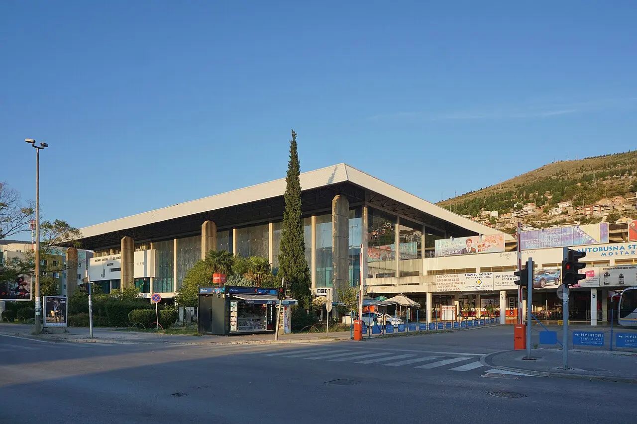 The modern concrete Mostar bus and railway station building in the north of the city under a clear sky, with the hillside behind