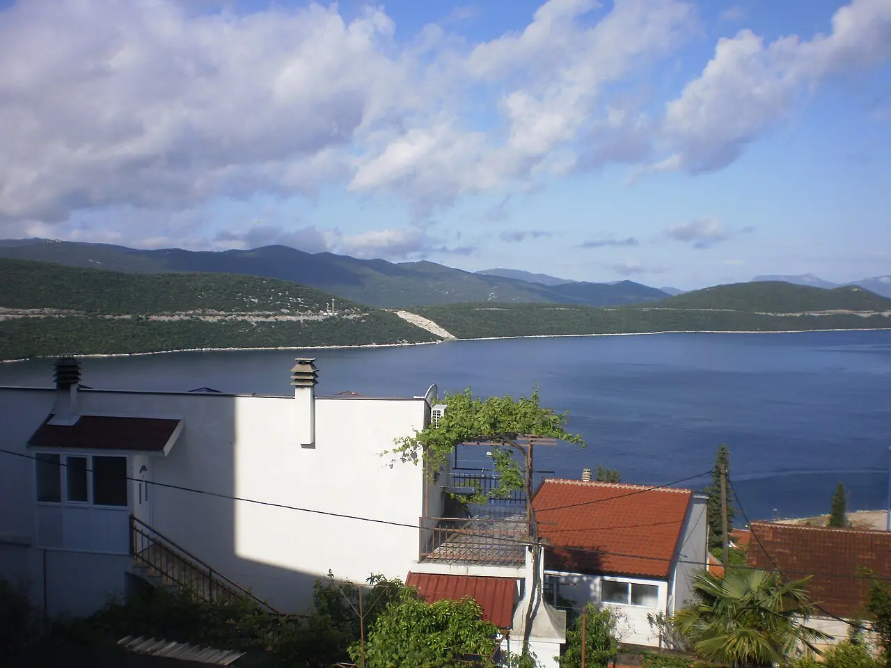 Sunny white apartment buildings and houses with a grapevine pergola on the Neum hillside above the blue bay
