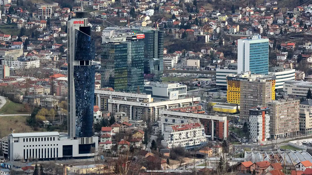 Aerial view of central Sarajevo with the black Avaz Twist Tower, glass office blocks and the yellow Holiday hotel, houses climbing the hillsides behind