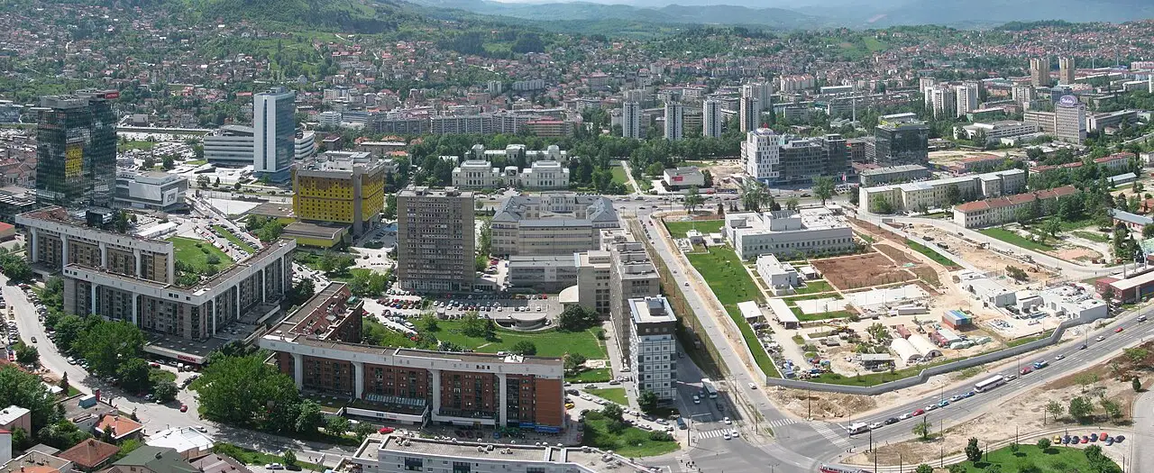 Wide view over the Marijin Dvor district of Sarajevo with modern towers, the yellow Holiday hotel and the National Museum in a valley ringed by hills