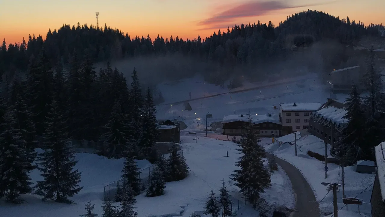 Dawn over the Jahorina ski resort, hotels and a mountain road below the pistes under an orange sky
